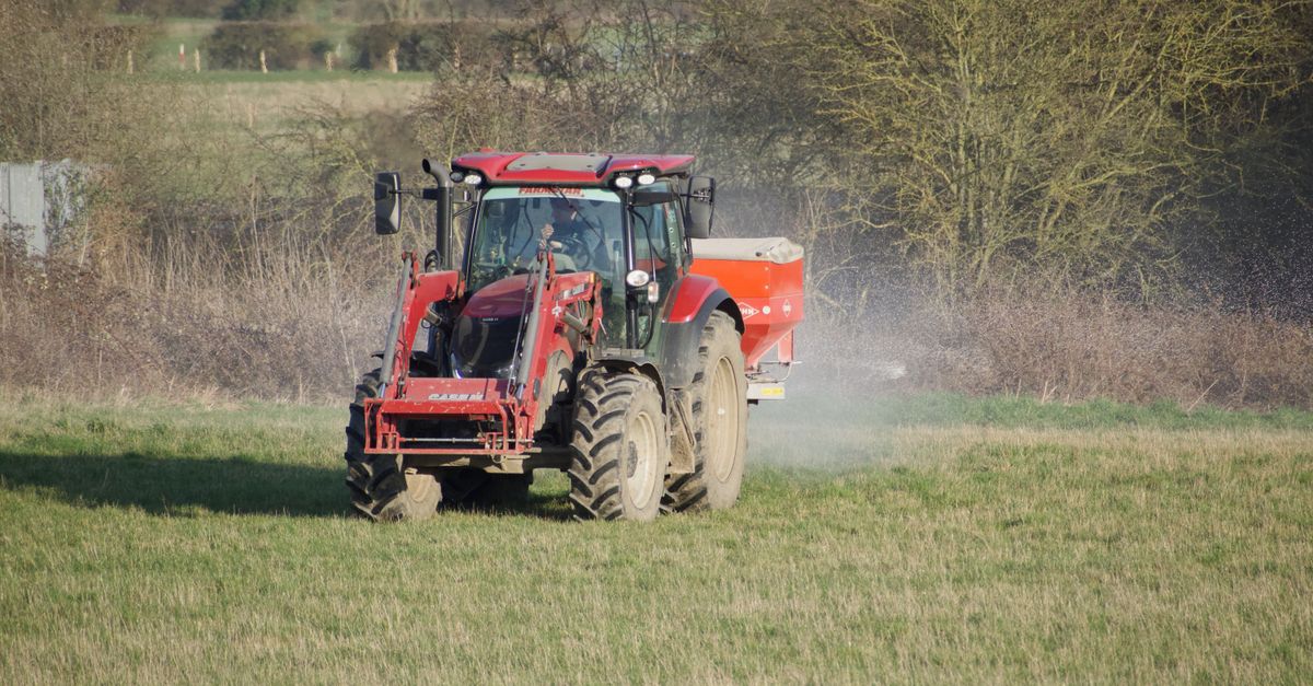 Red tractor working on a farm field spraying fertilizer during daytime agriculture work.